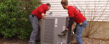 Two workers installing a new A/C unit outdoors
