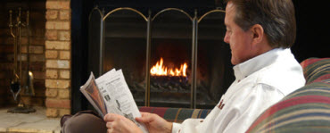 Man reading newspaper near fireplace